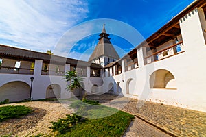 White stone wall of the courtyard with large arches and a wooden roof along the road with masonry in cloudy weather with blue