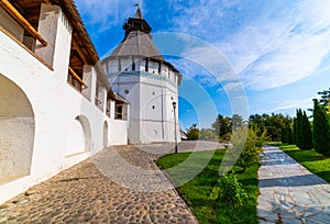 White stone wall of the courtyard with large arches and a wooden roof along the road with masonry in cloudy weather with blue