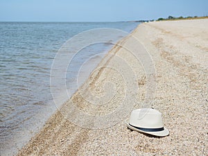 A white straw hat lies on the sand by the water. Sea beach on a summer sunny day. Sea vacation concept. Copy space.