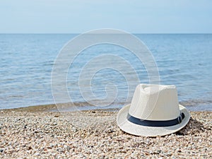 A white straw hat lies on the sand by the water. Sea beach on a summer sunny day. Sea vacation concept. Copy space.