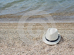 A white straw hat lies on the sand by the water. Sea beach on a summer sunny day. Sea vacation concept. Copy space.