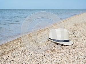 A white straw hat lies on the sand by the water. Sea beach on a summer sunny day. Sea vacation concept. Copy space.