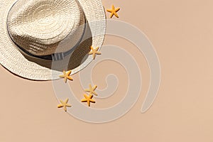 White straw wicker hat on a sand color background with yellow starfishes top view. hard shadows of the sun. minimal concept of