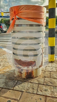 A white street garbage container is rusty at the bottom of the dog`s marks.