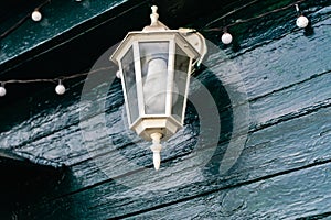 A white street lamp with its bulb turned off, hanging on a dark green wooden crowbar