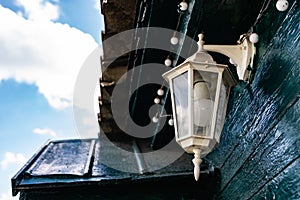 A white street lamp with its bulb turned off, hanging on a dark green wooden crowbar