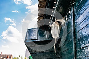 A white street lamp with its bulb turned off, hanging on a dark green wooden crowbar