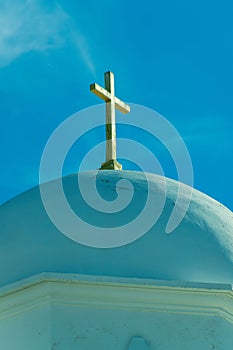 White stucco or cement church dome with visible cross on top and whispy cloud blue sky background in intense lighting
