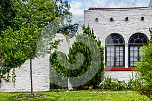 White stucco house detail with arched gate in attached stucco wall - iron arched windows and gable vent tubes