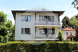 White suburban family house with two front balconies and open windows surrounded with hedge and trees