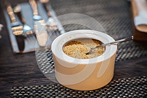 White sugar bowl with brown sugar and spoon on a table