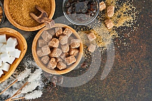 White sugar, cane sugar cubes, caramel in bamboo bowl on dark brown table concrete background. Assorted different types of sugar.