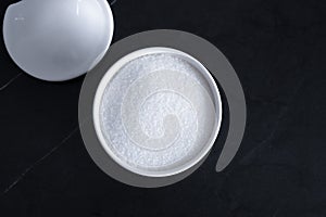 White sugar granules in a bowl and with a lid on a black kitchen table