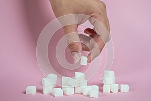 White sugar loaf on the pink floor and the male hand holding the sugar cube