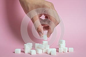 White sugar loaf on the pink floor and the male hand holding the sugar cube