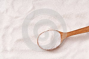 white sugar in wooden spoon on the sugar background