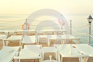 White sun loungers on the background of the sea, stand on the pier at dawn. orange lifebuoys.