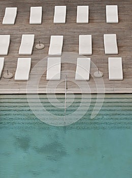 White sun-loungers and deckchairs next to the swimming pool with crystal blue water