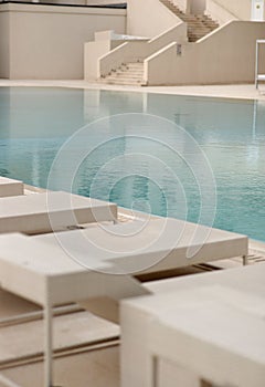 White sun-loungers and deckchairs next to the swimming pool with crystal blue water