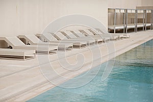 White sun-loungers and deckchairs next to the swimming pool with crystal blue water