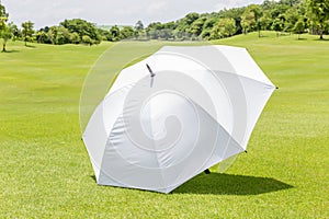 The white sun umbrella place on green grass golf course using for sun protection.