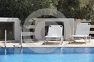 White sunbeds and swimming pool in summer