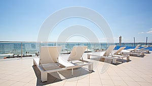 White sunbeds at the terrace of a hotel near the tropical beach. A lot of white deck chairs near the sea beach. Summertime.