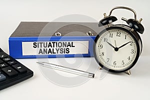 On a white surface, an alarm clock calculator and a folder with the inscription - Situational Analysis