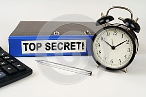 On a white surface, an alarm clock calculator and a folder with the inscription - Top Secret