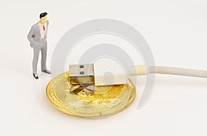 On a white surface are a bitcoin cord with USB and a miniature human figure.