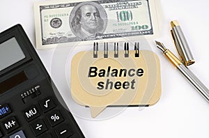 On a white surface, a calculator, dollars, a pen and a sign with the inscription - Balance sheet