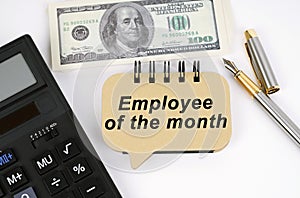 On a white surface, a calculator, dollars, a pen and a sign with the inscription - Employee of the Month