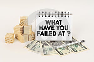 On a white surface, cubes, dollars, a pen and a notepad with the inscription - What Have You Failed At