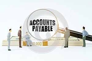 On a white surface, a dollar, figurines of people and a magnifying glass with the inscription - Accounts Payable