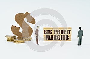 On a white surface, a dollar symbol, a figurine of businessmen and a wooden sign with the inscription Big Profit Margins