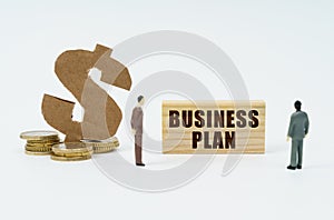 On a white surface, a dollar symbol, a figurine of businessmen and a wooden sign with the inscription - BUSINESS PLAN