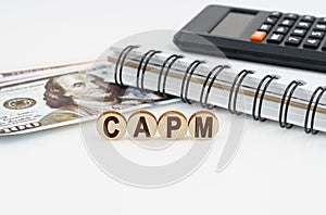 On a white surface are dollars, a notebook, a calculator and wooden circles with the inscription - CAPM photo