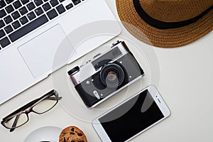 White surface with laptop, hat, eyeglasses, smartphone, camera a