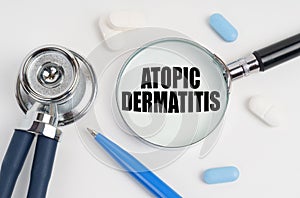 On a white surface lie pills, a pen, a stethoscope and a magnifying glass with the inscription - Atopic Dermatitis