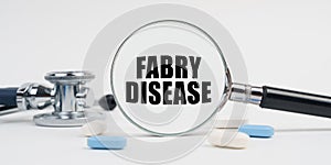 On a white surface lie pills, a stethoscope and a magnifying glass with the inscription - FABRY DISEASE