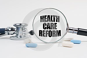 On a white surface lie pills, a stethoscope and a magnifying glass with the inscription - HEALTH CARE REFORM