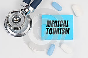 On a white surface lie pills, a stethoscope and stickers with the inscription - MEDICAL TOURISM