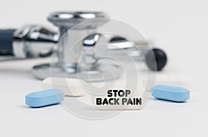 On a white surface lie pills, a stethoscope and a tablet with the inscription - STOP BACK PAIN
