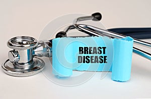 On a white surface lies a stethoscope and a blue roll of paper with the inscription - BREAST DISEASE