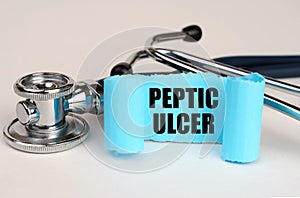 On a white surface lies a stethoscope and a blue roll of paper with the inscription - Peptic ulcer
