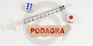 On a white surface lies a syringe, dice and a piece of paper with the inscription - podagra