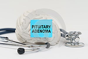 On a white surface next to the stethoscope lies a brain on which a sticker with the inscription - Pituitary adenoma