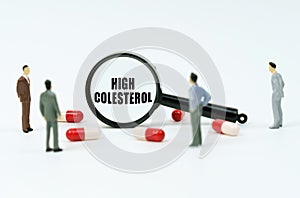 On a white surface are pills, figurines of people and a magnifying glass with the inscription - High Colesterol photo