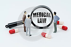 On a white surface are pills, miniature figures of people and a magnifying glass with the inscription - MEDICAL LAW