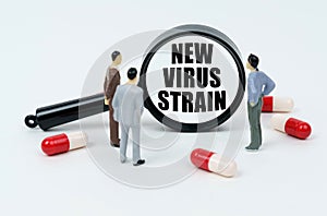 On a white surface are pills, miniature figures of people and a magnifying glass with the inscription - new virus strain